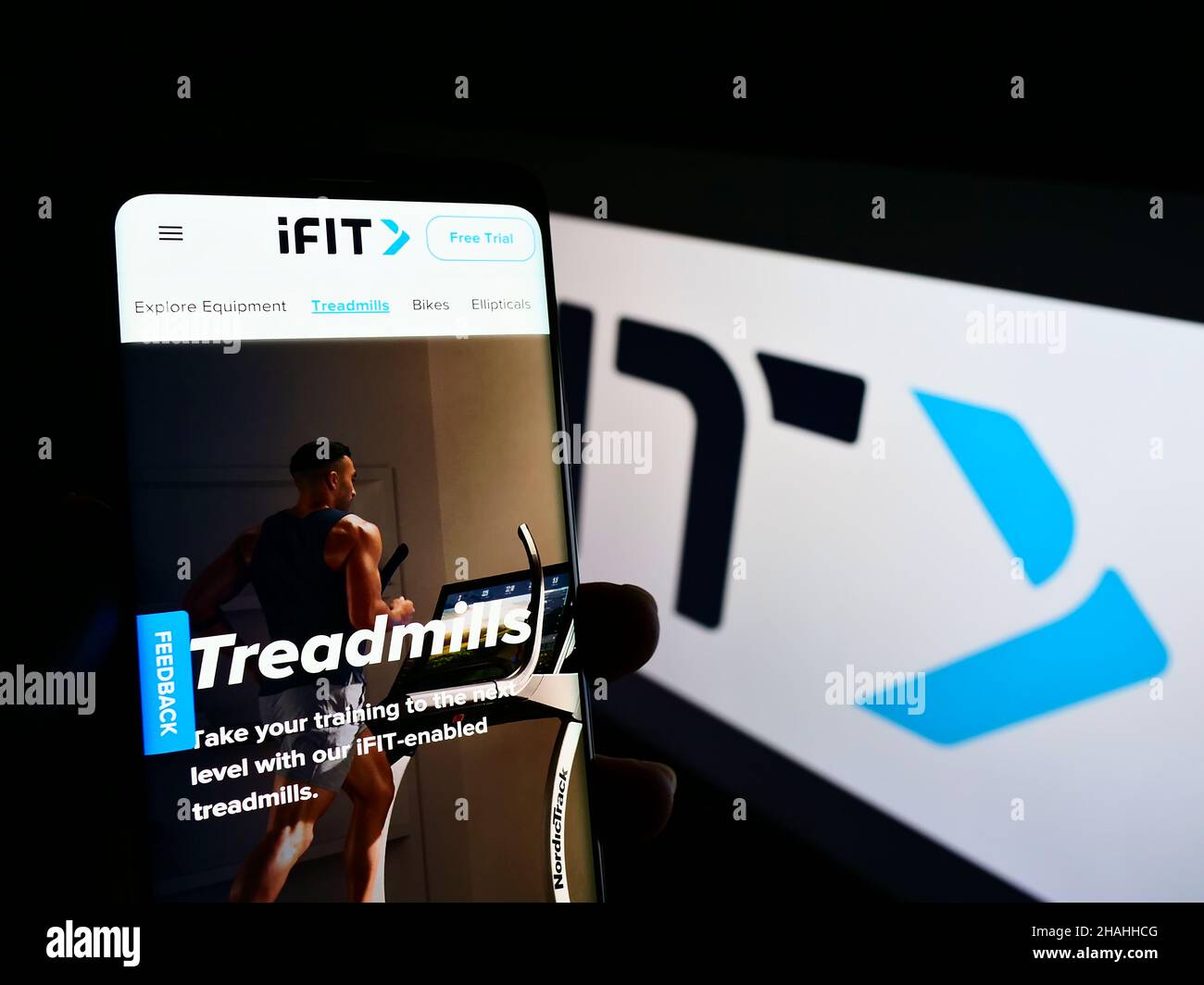 Person holding cellphone with webpage of US fitness company iFIT Inc. on screen in front of business logo. Focus on center of phone display. Stock Photo