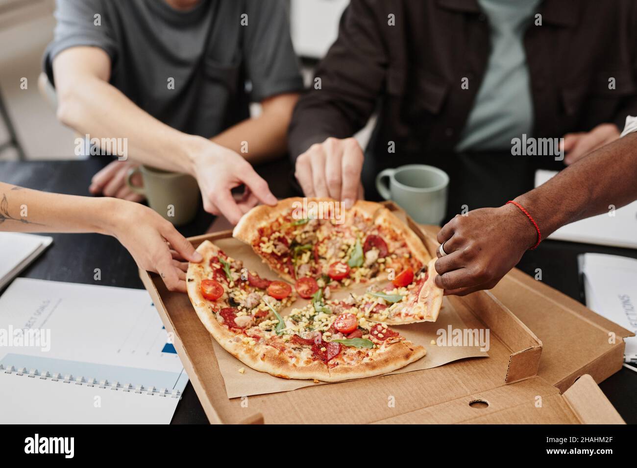 Close-up of business people taking pieces of pizza during lunch while sitting at the table at office Stock Photo