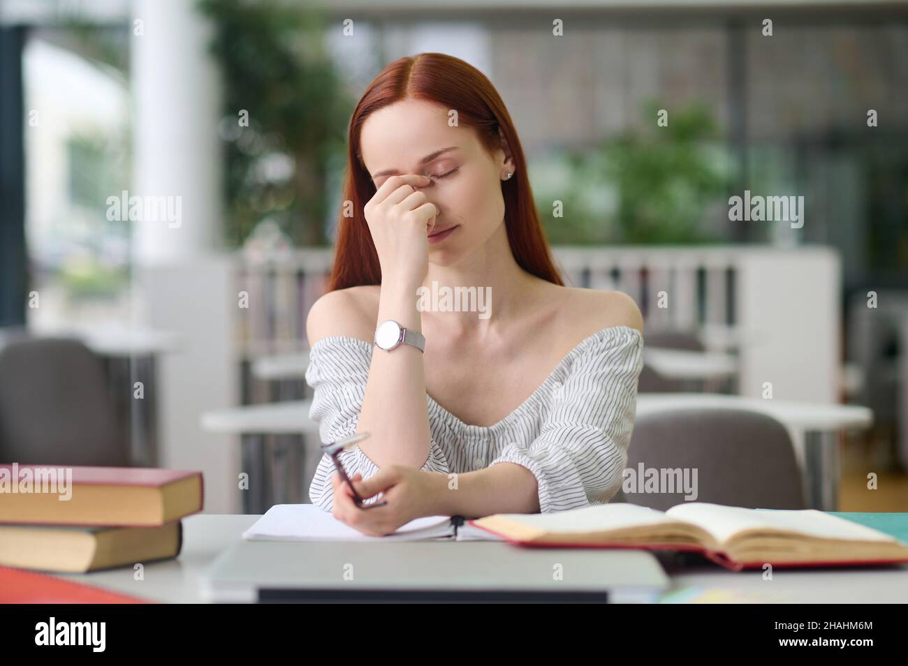 Tired woman with closed eyes sitting at table Stock Photo