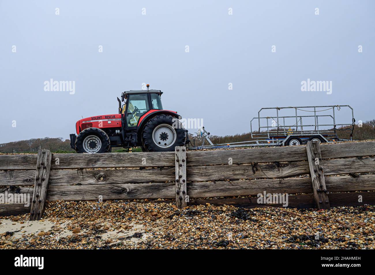 Solent rescue red massey ferguson tractor and rescue boat trailer parked on pebble bank at Lepe beach, weathered wooden storm fence. Lepe Country Park Stock Photo