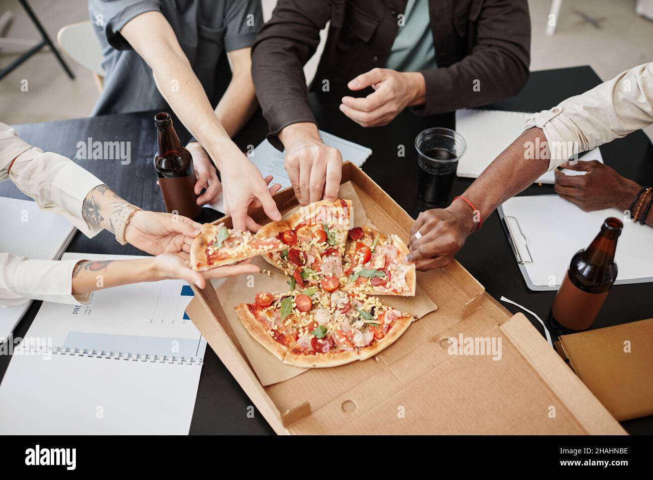 Close-up of colleagues taking slices of pizza while celebrating with beer at the table at office Stock Photo
