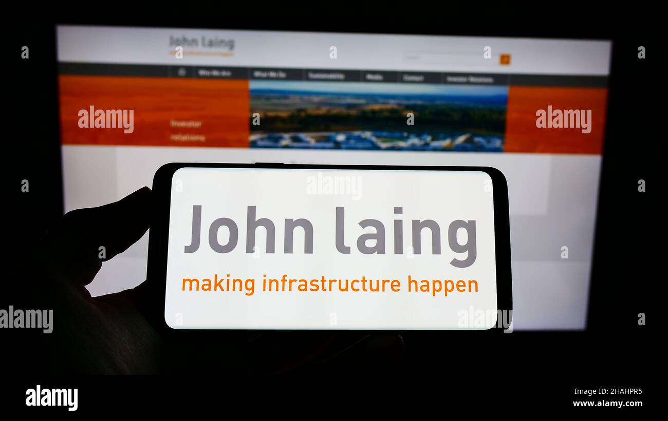 Person holding cellphone with logo of British company John Laing Group Limited on screen in front of business webpage. Focus on phone display. Stock Photo