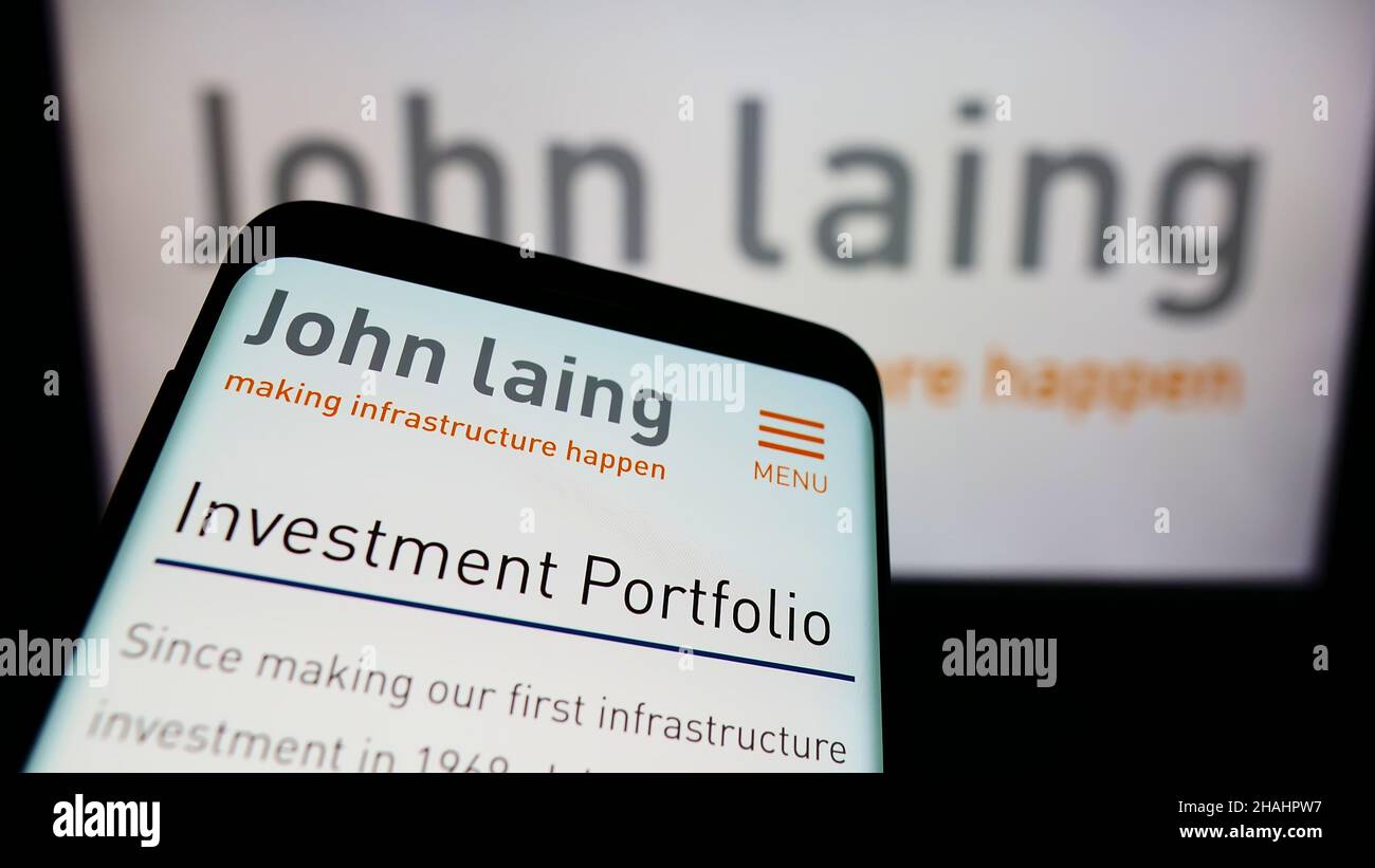 Mobile phone with webpage of British company John Laing Group Limited on screen in front of business logo. Focus on top-left of phone display. Stock Photo