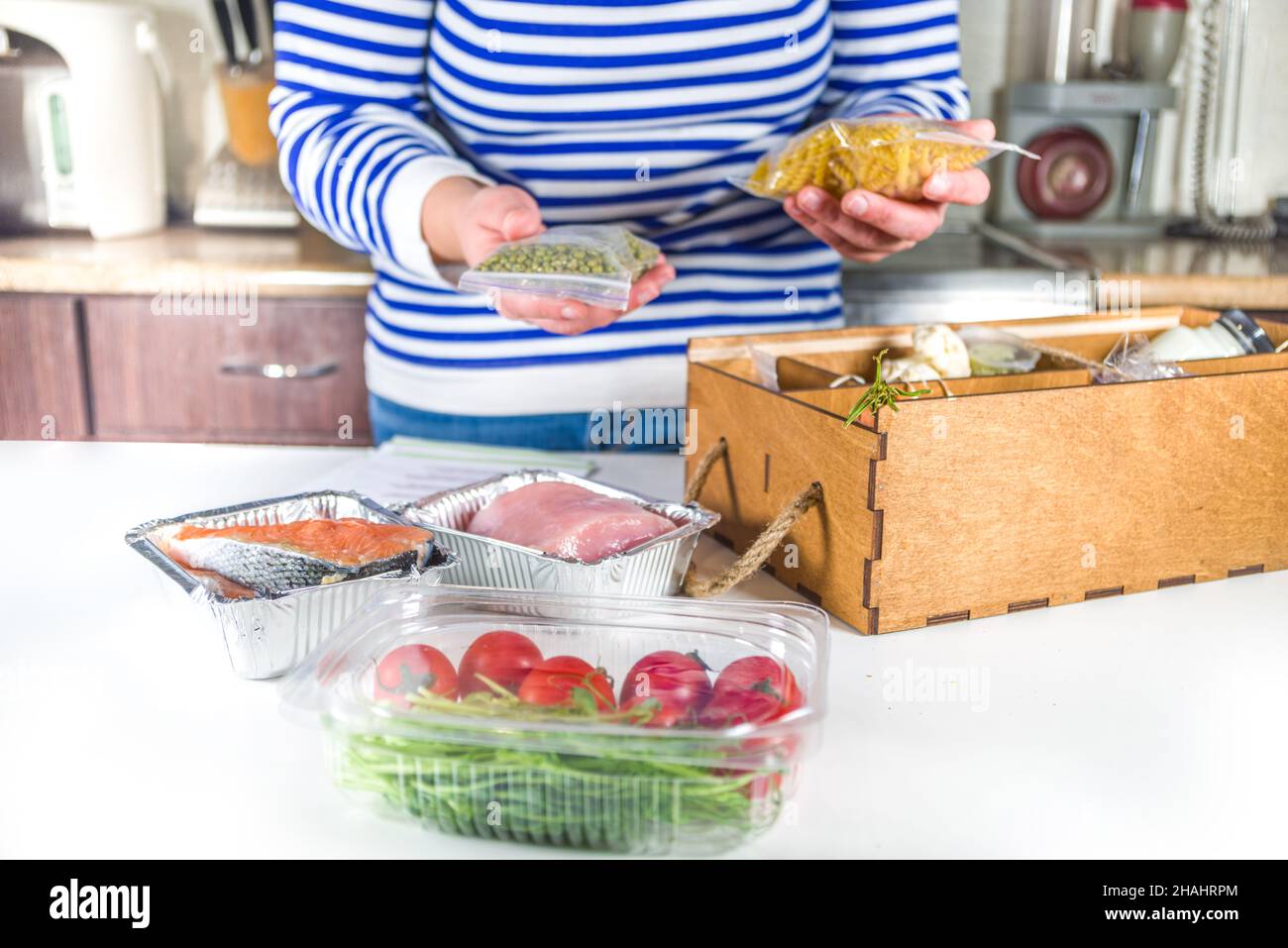 Caucasian woman take apart box with delivery of ingredients, recipes. Meal Kit Delivery Concept. Set various healthy foods with recipes for cooking. O Stock Photo
