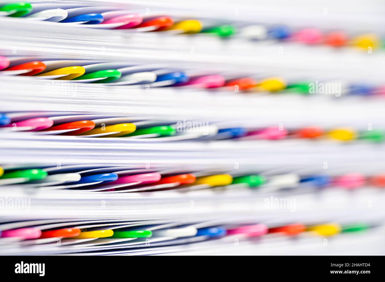 Colorful paperclips in a stack of files and papers. Office work, bureaucracy or red tape concept. Stock Photo