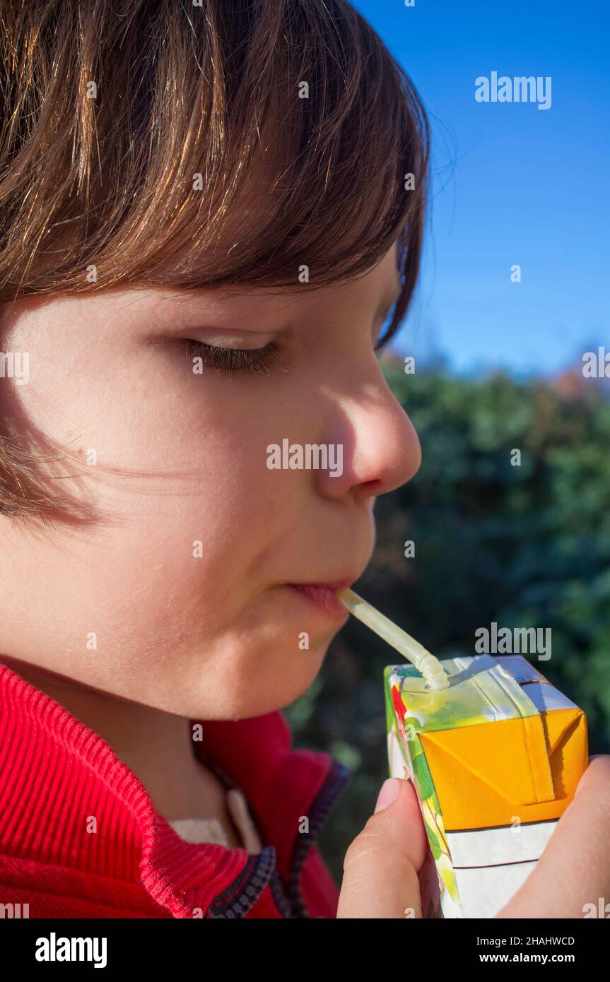 Child boy drinking sweetened juice fruit juice from brick. Fruit juice