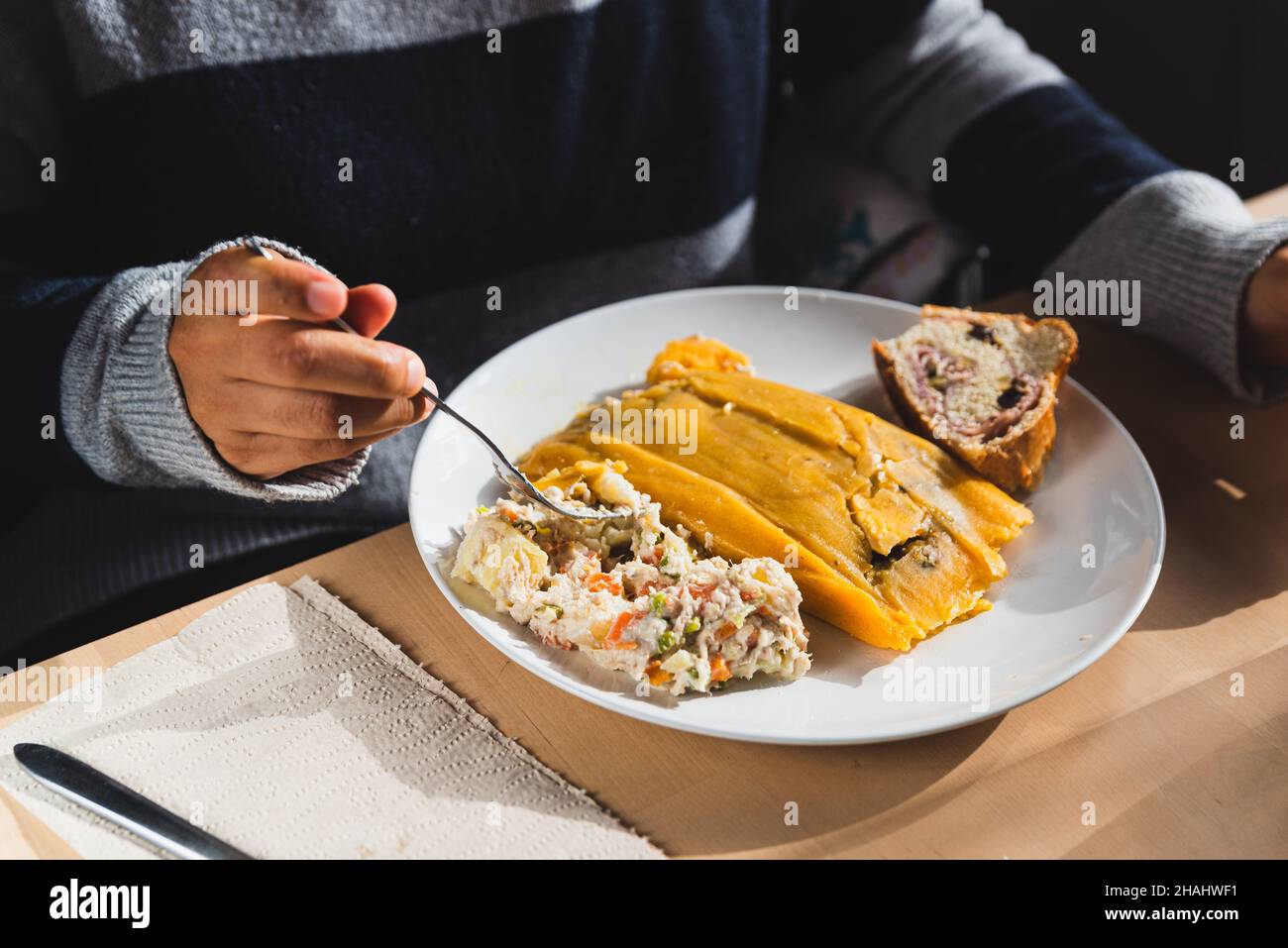 woman eating traditional venezuelan christmas dish with hallacas, pan de jamon or ham bread, and mixed salad, with cutlery and ready. traditional dish Stock Photo