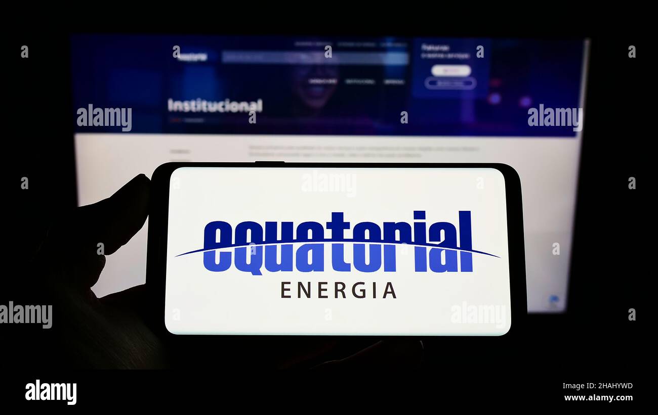 Person holding mobile phone with logo of Brazilian energy company Equatorial Energia S.A. on screen in front of web page. Focus on phone display. Stock Photo