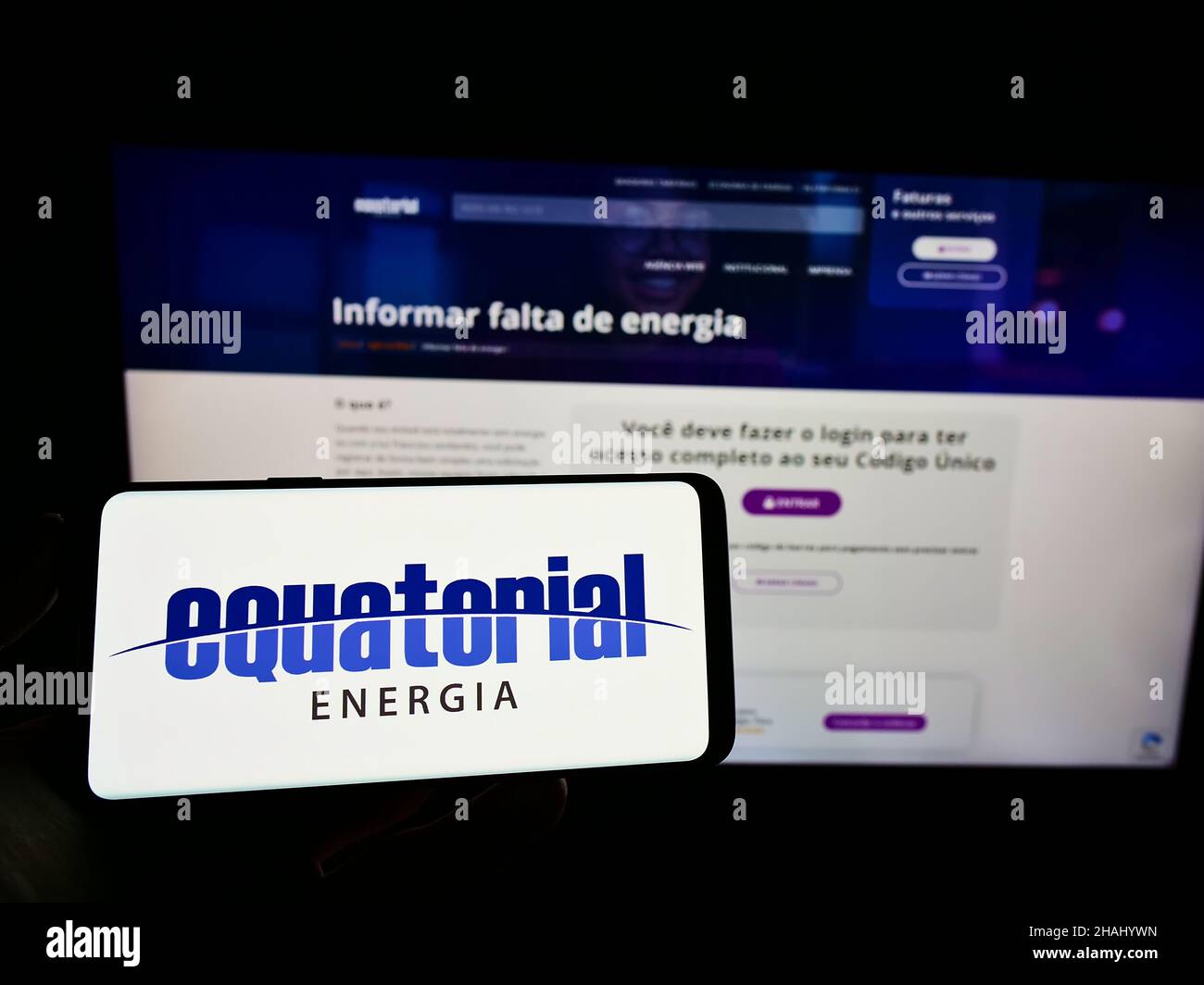 Person holding cellphone with logo of Brazilian energy company Equatorial Energia S.A. on screen in front of webpage. Focus on phone display. Stock Photo
