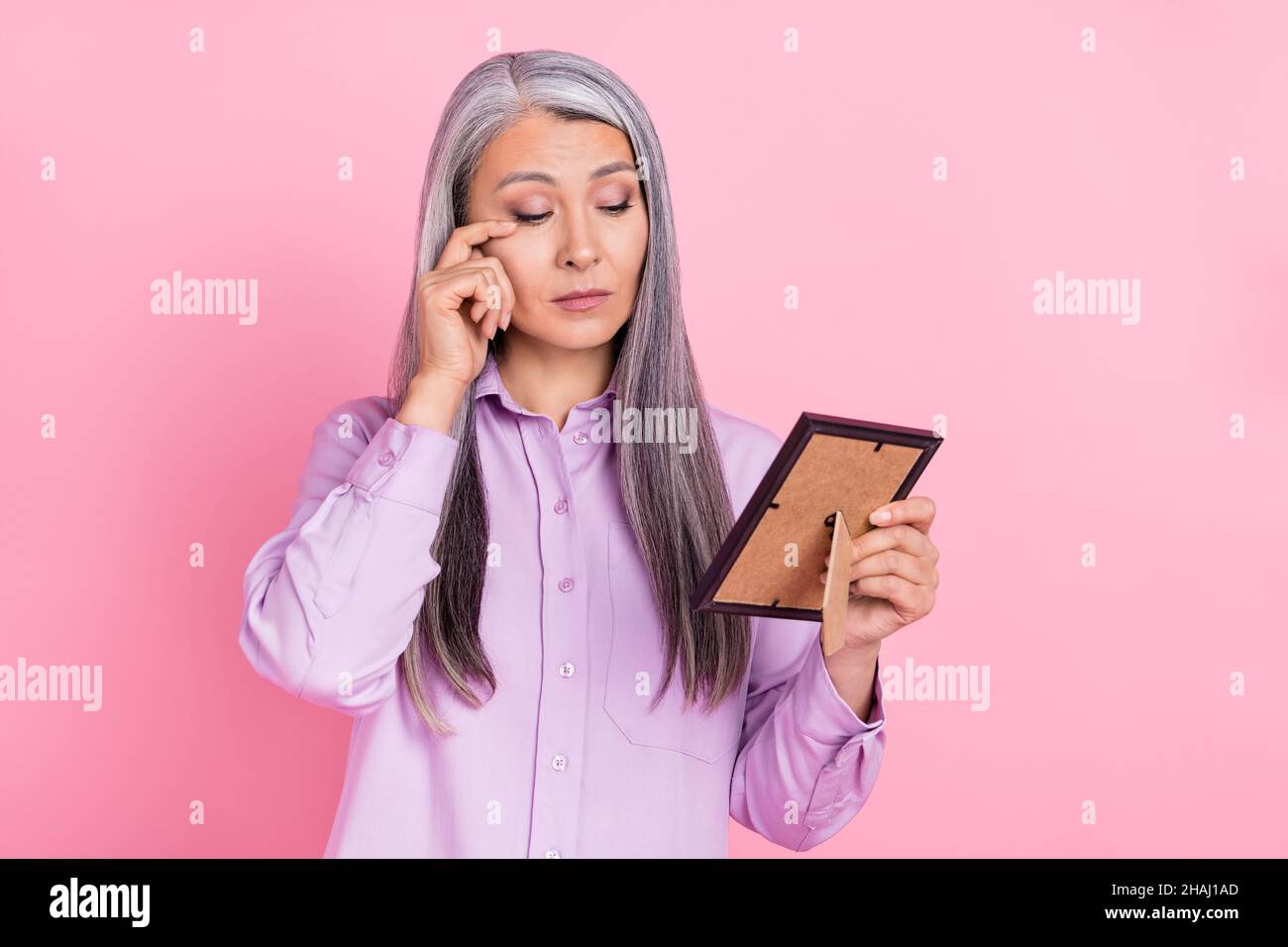 Portrait of attractive sad sullen gray-haired woman looking at photo crying isolated over pink pastel color background Stock Photo