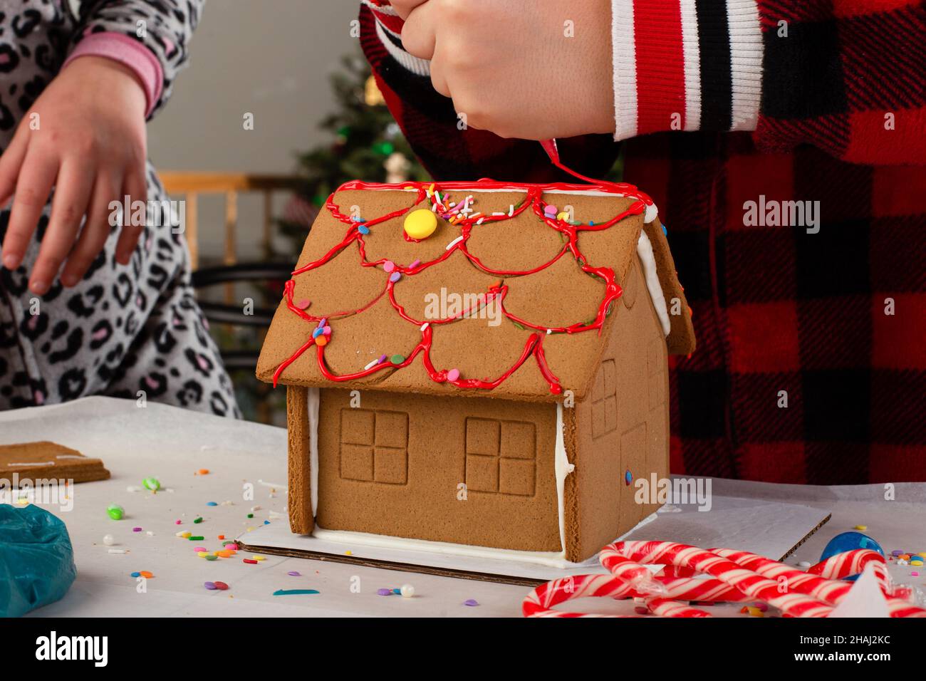 Kids assembling and decorating a gingerbread house at Christmas time. Christmas family tradition, Christmas crafts. Stock Photo