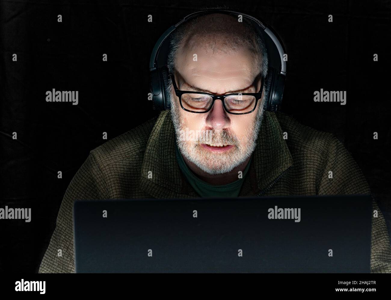 A white grey bearded male listening to music through headphones. low key lighting. Stock Photo