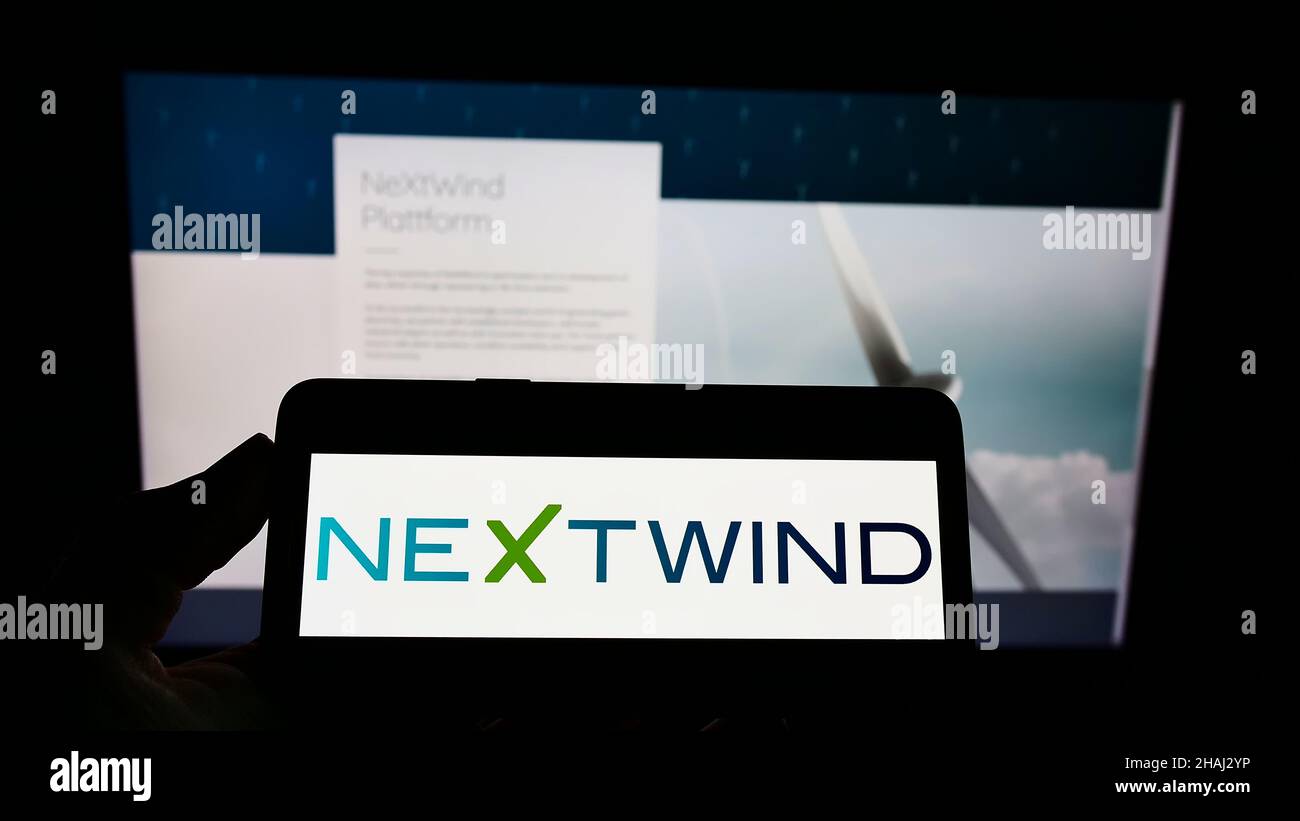 Person holding cellphone with logo of wind energy company NeXtWind Management GmbH on screen in front of business webpage. Focus on phone display. Stock Photo