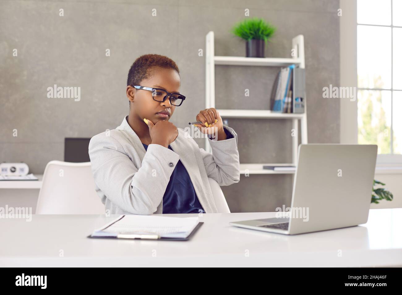 Black woman sitting at office desk, looking at laptop screen, reading and thinking Stock Photo