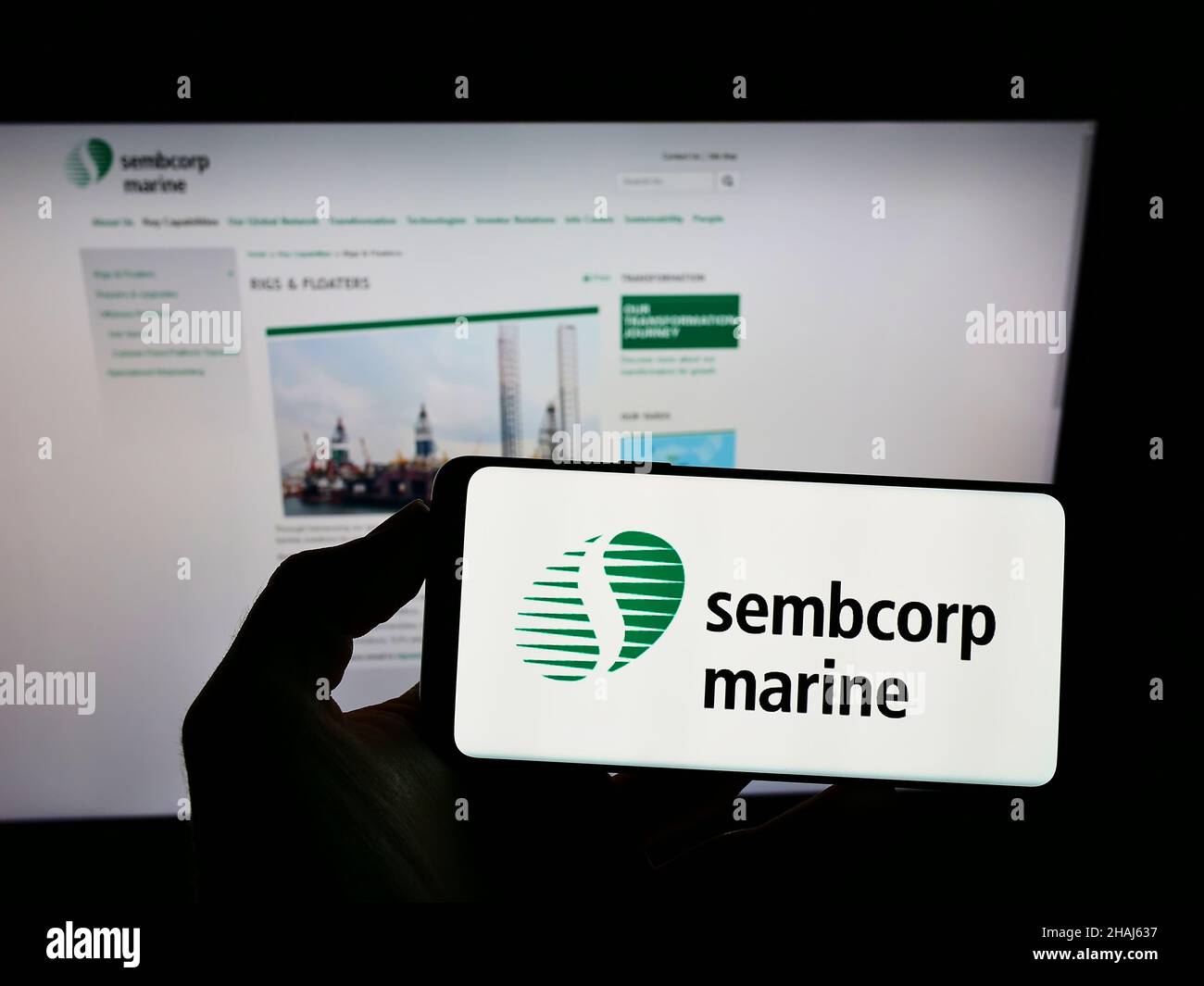 Person holding smartphone with logo of Singaporean company Sembcorp Industries Ltd on screen in front of website. Focus on phone display. Stock Photo