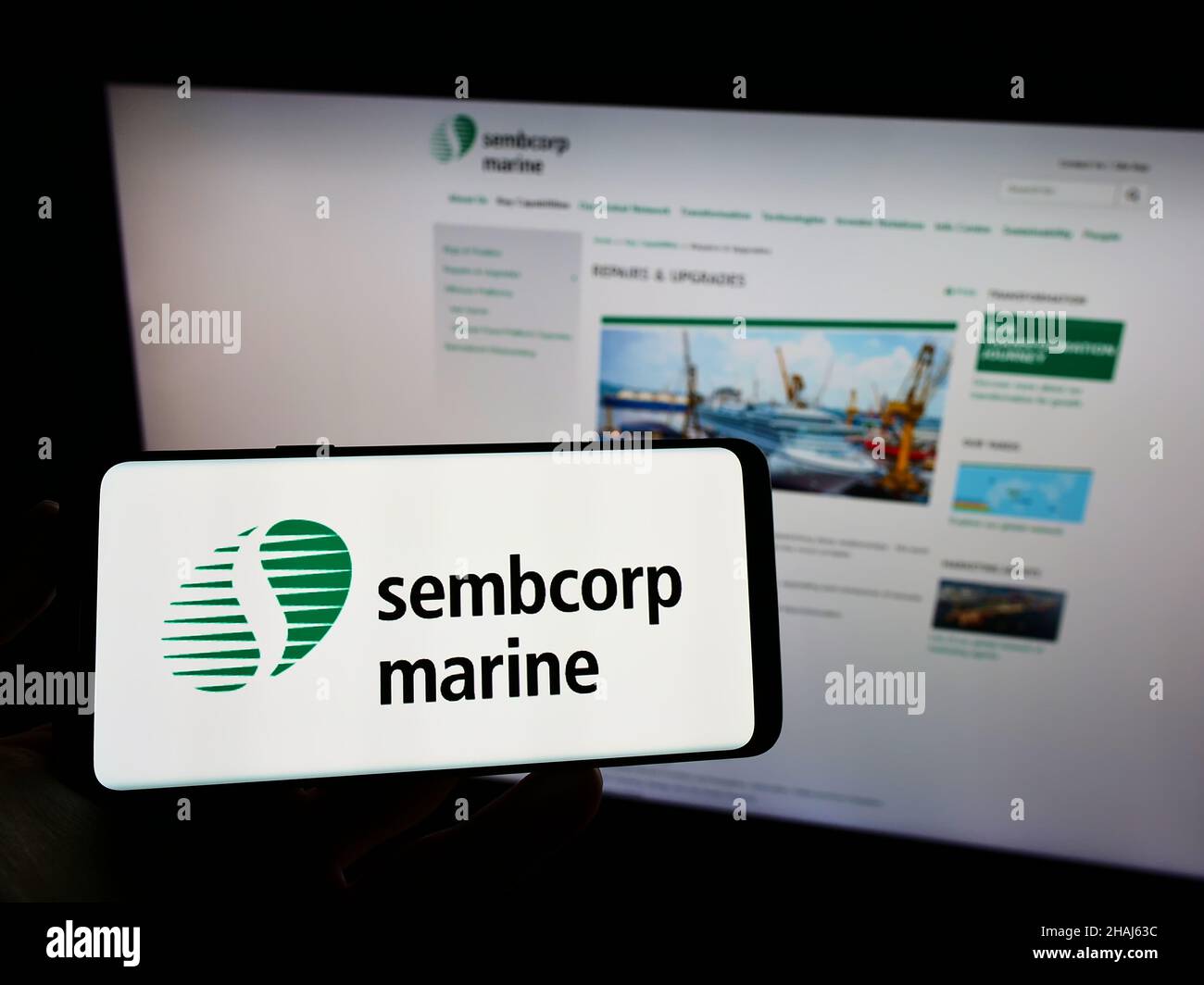 Person holding mobile phone with logo of Singaporean company Sembcorp Industries Ltd on screen in front of web page. Focus on phone display. Stock Photo