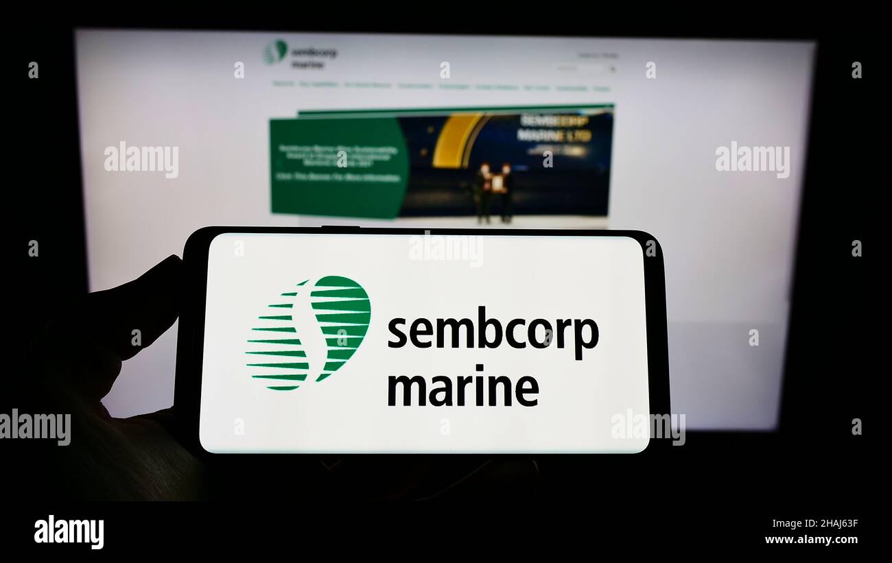 Person holding cellphone with logo of Singaporean company Sembcorp Industries Ltd on screen in front of business webpage. Focus on phone display. Stock Photo