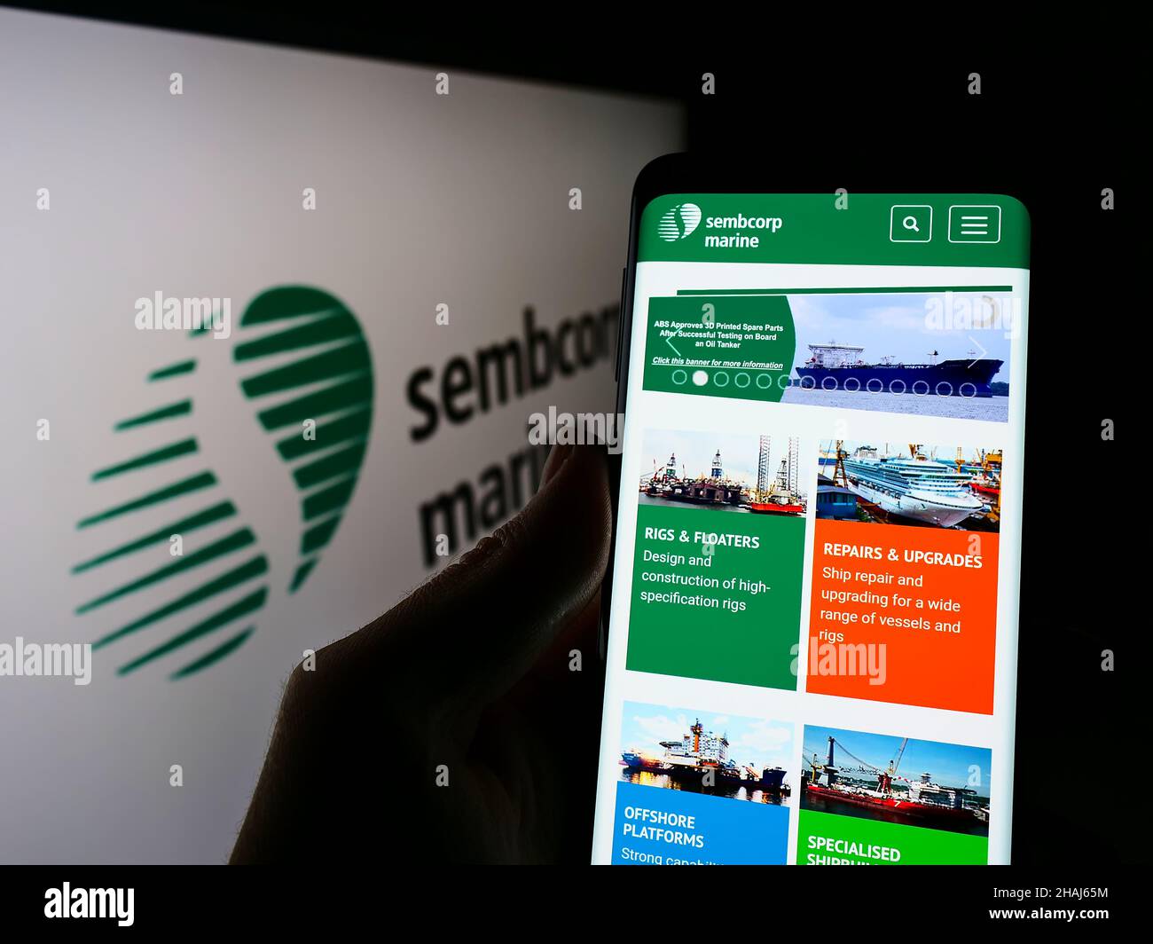 Person holding smartphone with website of Singaporean company Sembcorp Industries Ltd on screen in front of logo. Focus on center of phone display. Stock Photo