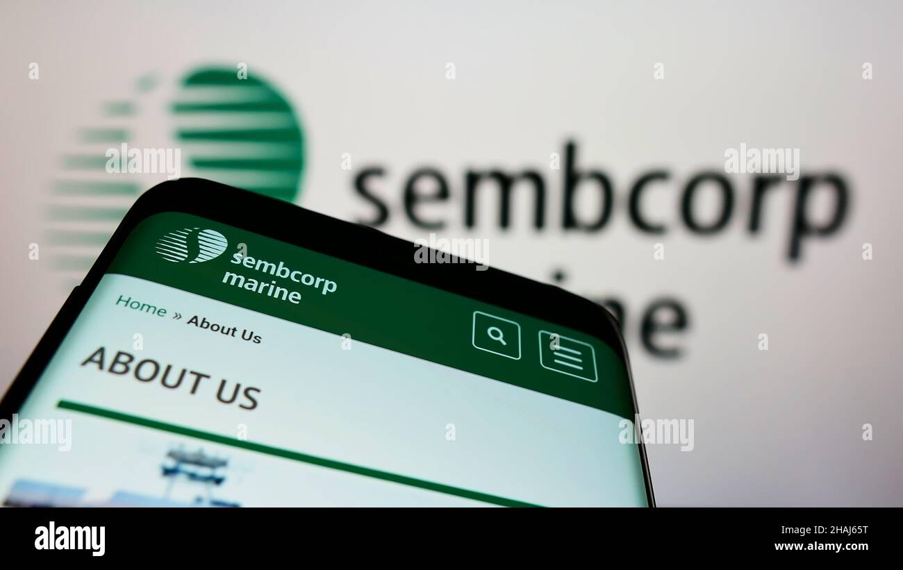 Mobile phone with webpage of Singaporean company Sembcorp Industries Ltd on screen in front of business logo. Focus on top-left of phone display. Stock Photo