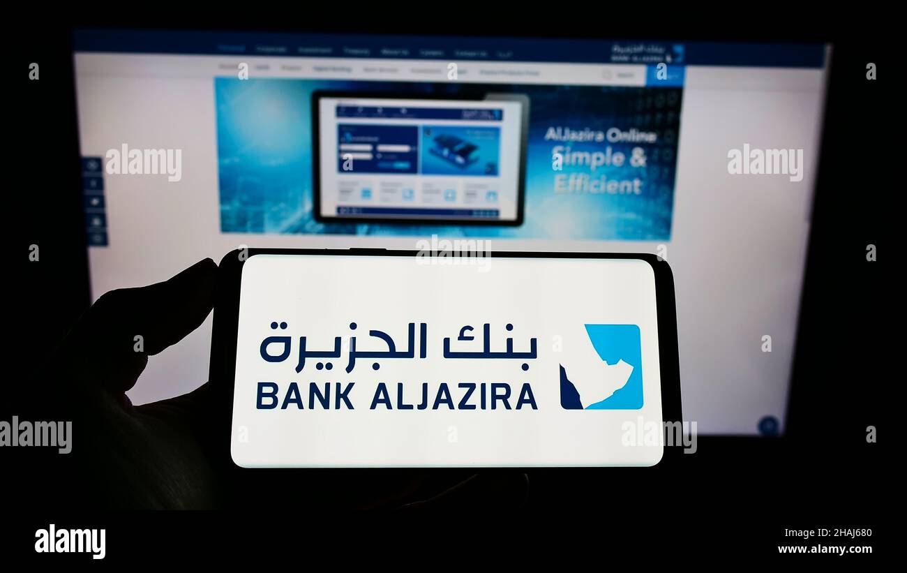 Person holding cellphone with logo of Saudi Arabian company Bank Aljazira (BAJ) on screen in front of business webpage. Focus on phone display. Stock Photo
