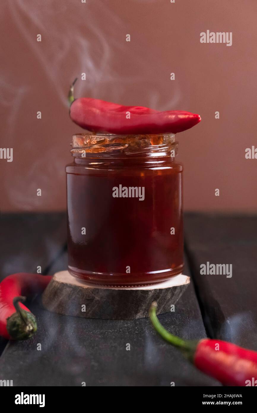 Hot pepper jam with steam coming from it on wooden table and spicy peppers on table Stock Photo