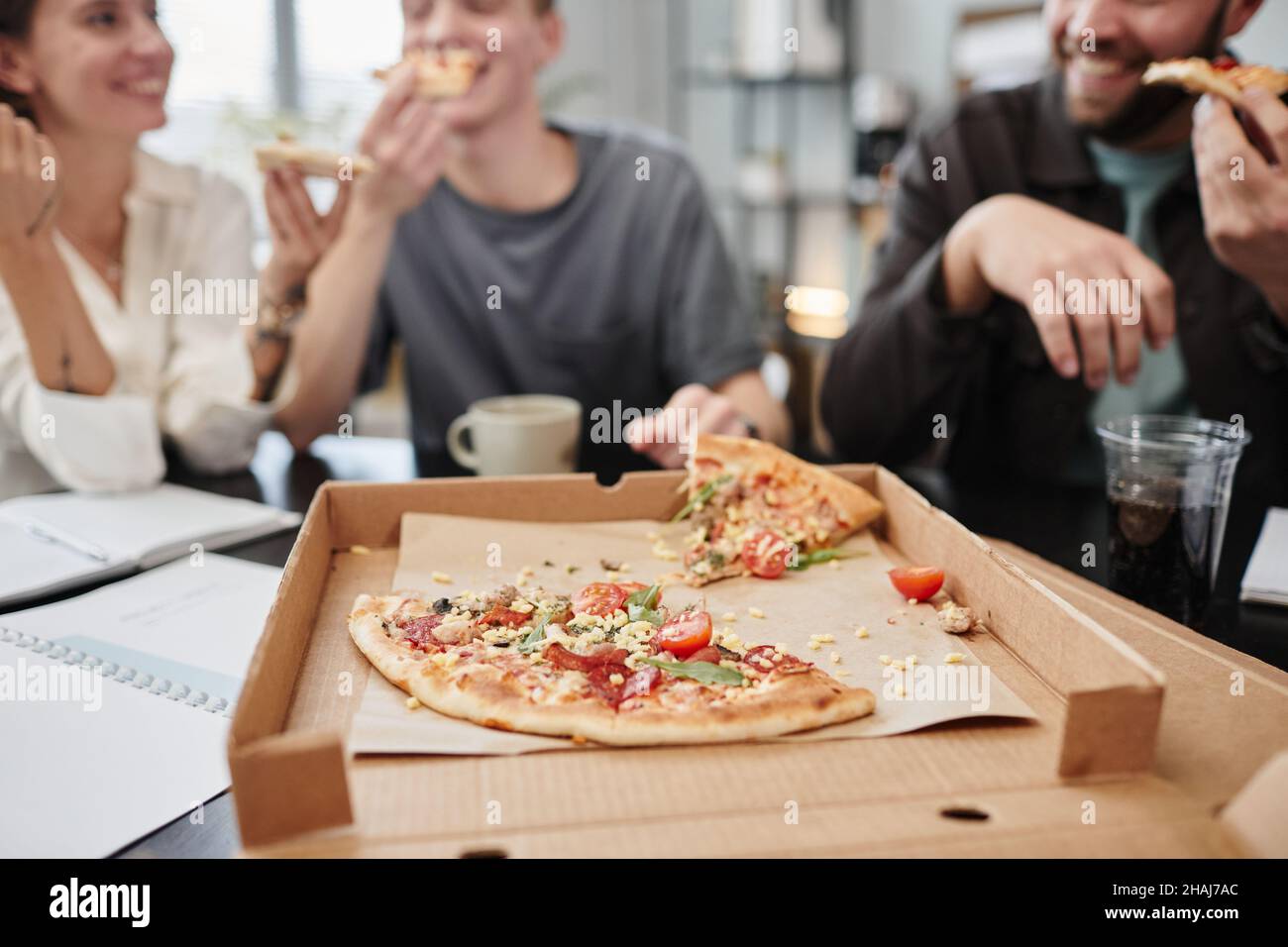 Close-up of fresh pizza in the opened box with business people having lunch at the table in the background Stock Photo