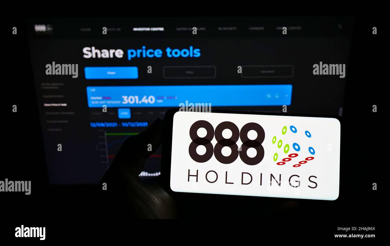 Person holding mobile phone with logo of online gambling company 888 Holdings plc on screen in front of business web page. Focus on phone display. Stock Photo