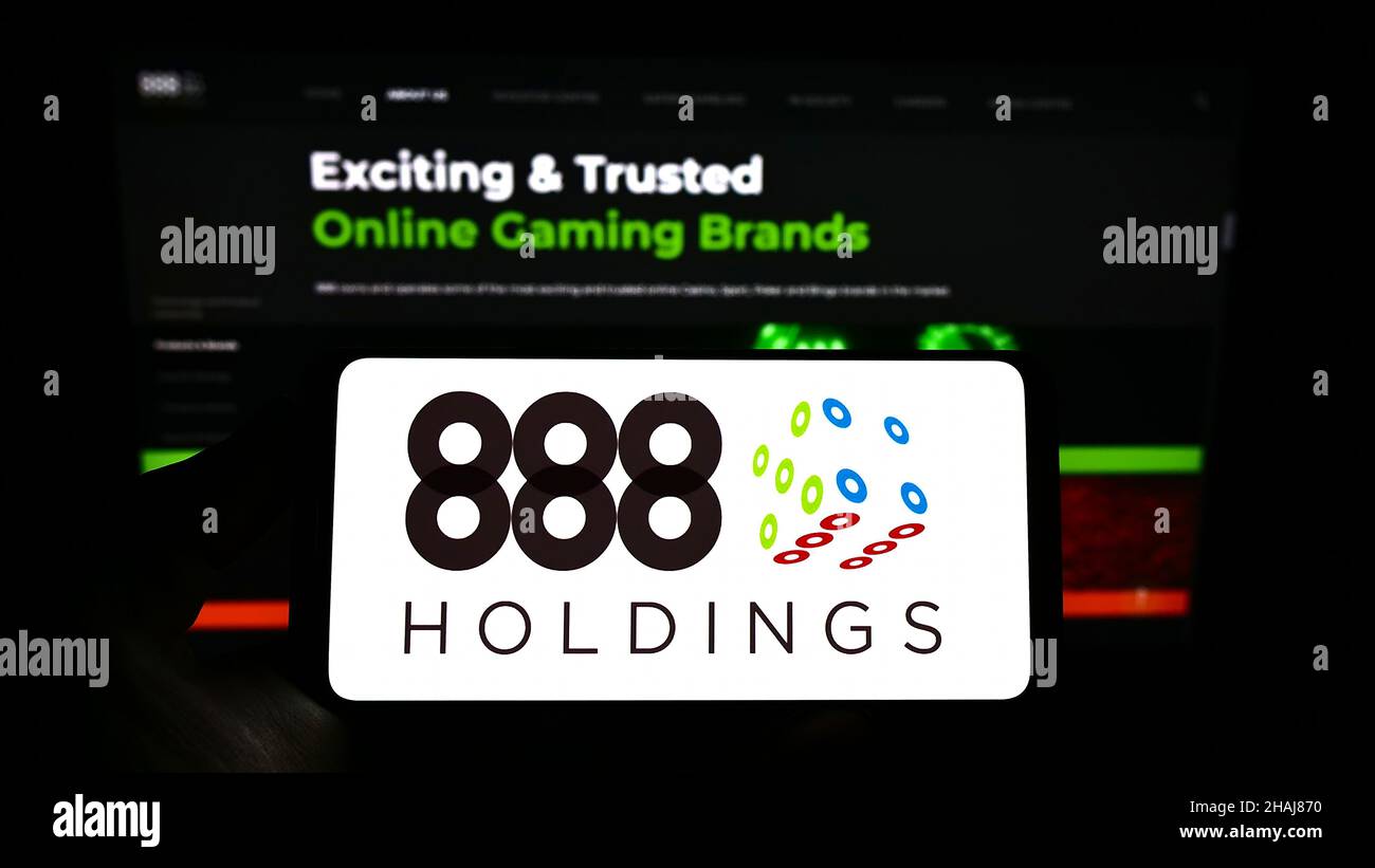 Person holding cellphone with logo of online gambling company 888 Holdings plc on screen in front of business webpage. Focus on phone display. Stock Photo