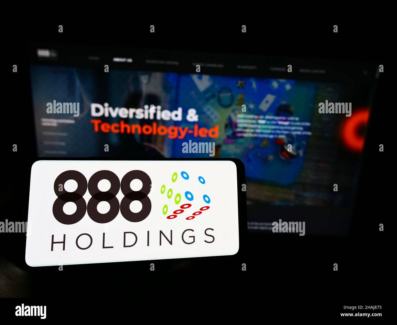 Person holding smartphone with logo of online gambling company 888 Holdings plc on screen in front of website. Focus on phone display. Stock Photo