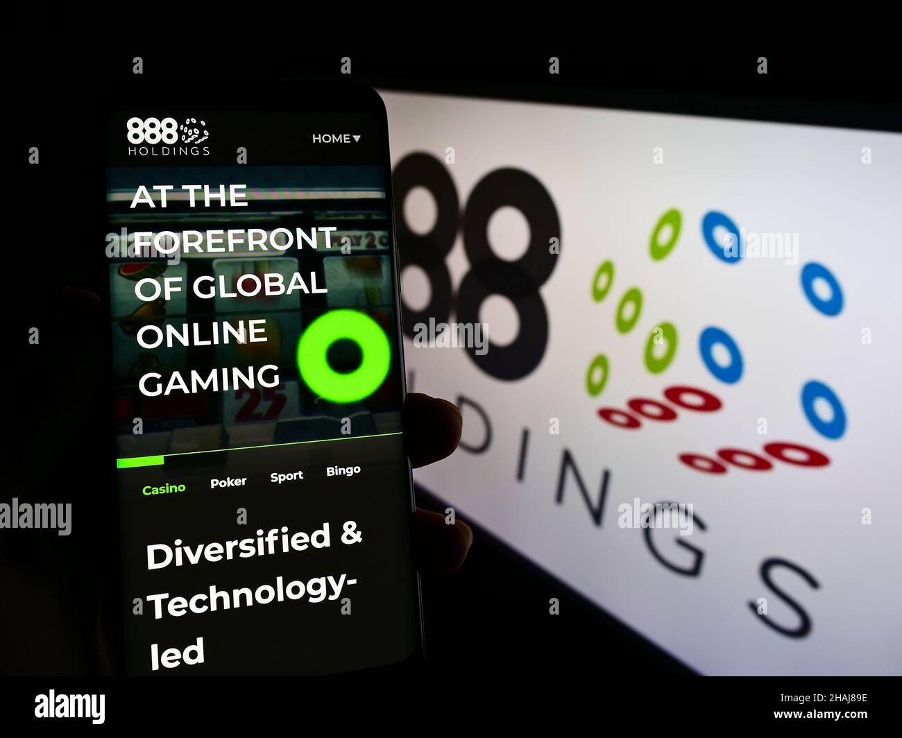Person holding smartphone with website of online gambling company 888 Holdings plc on screen in front of logo. Focus on center of phone display. Stock Photo