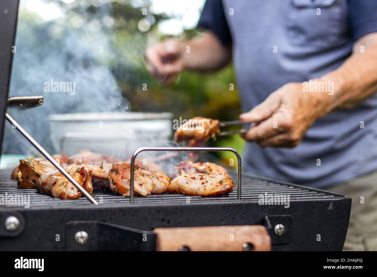 Senior man preparing barbecue grill for garden party. Selective focus at grilled chicken meat Stock Photo