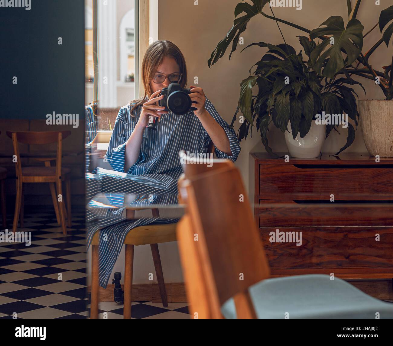 Minsk, Belarus - 22 October 2021 Woman taking photo of self, reflecting in mirror in modern cafe with daylight and green plants. Photographer with professional camera. Stock Photo