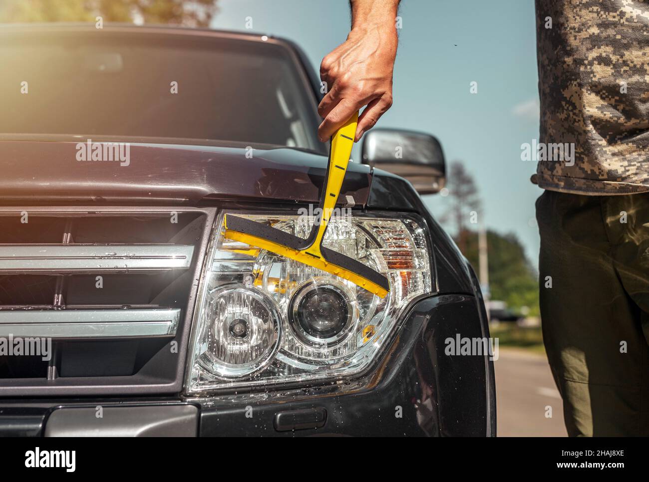 Driver cleaning shiny headlights of new black car, close up. Stock Photo