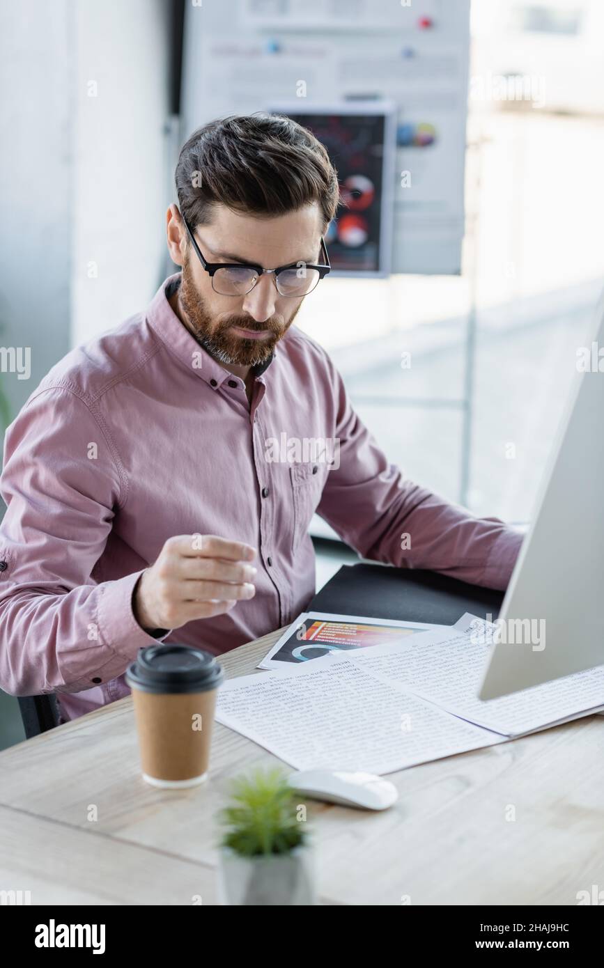 Businessman working with papers and computer near coffee to go in ...