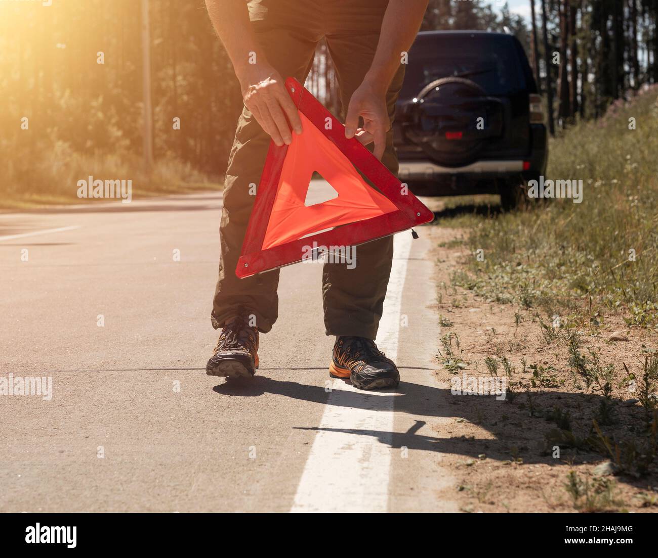 Male hands closeup putting red triangle caution sign on road side near broken car in summer. Stock Photo