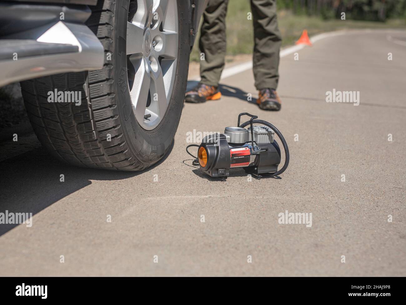 Portable tire pump for inflating car wheel on road. Tyre inflator air compressor with manometer. Stock Photo