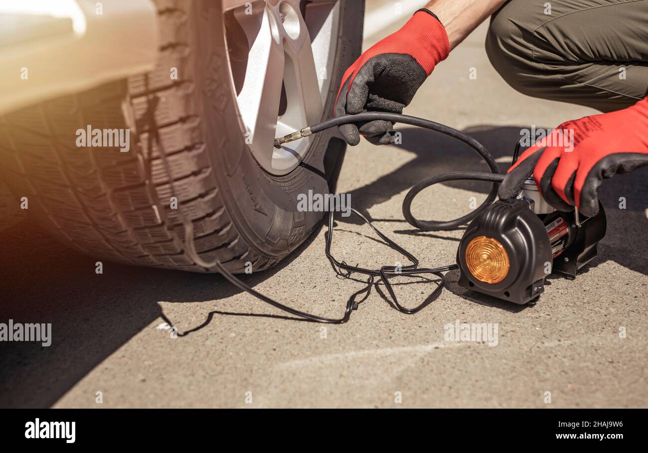 Tire pump inflating car wheel. Tyre inflator in male hands, checking pressure with manometer. Stock Photo