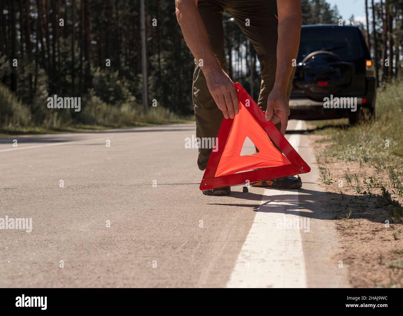 Male hands closeup putting red triangle caution sign on road side near broken car in summer. Stock Photo