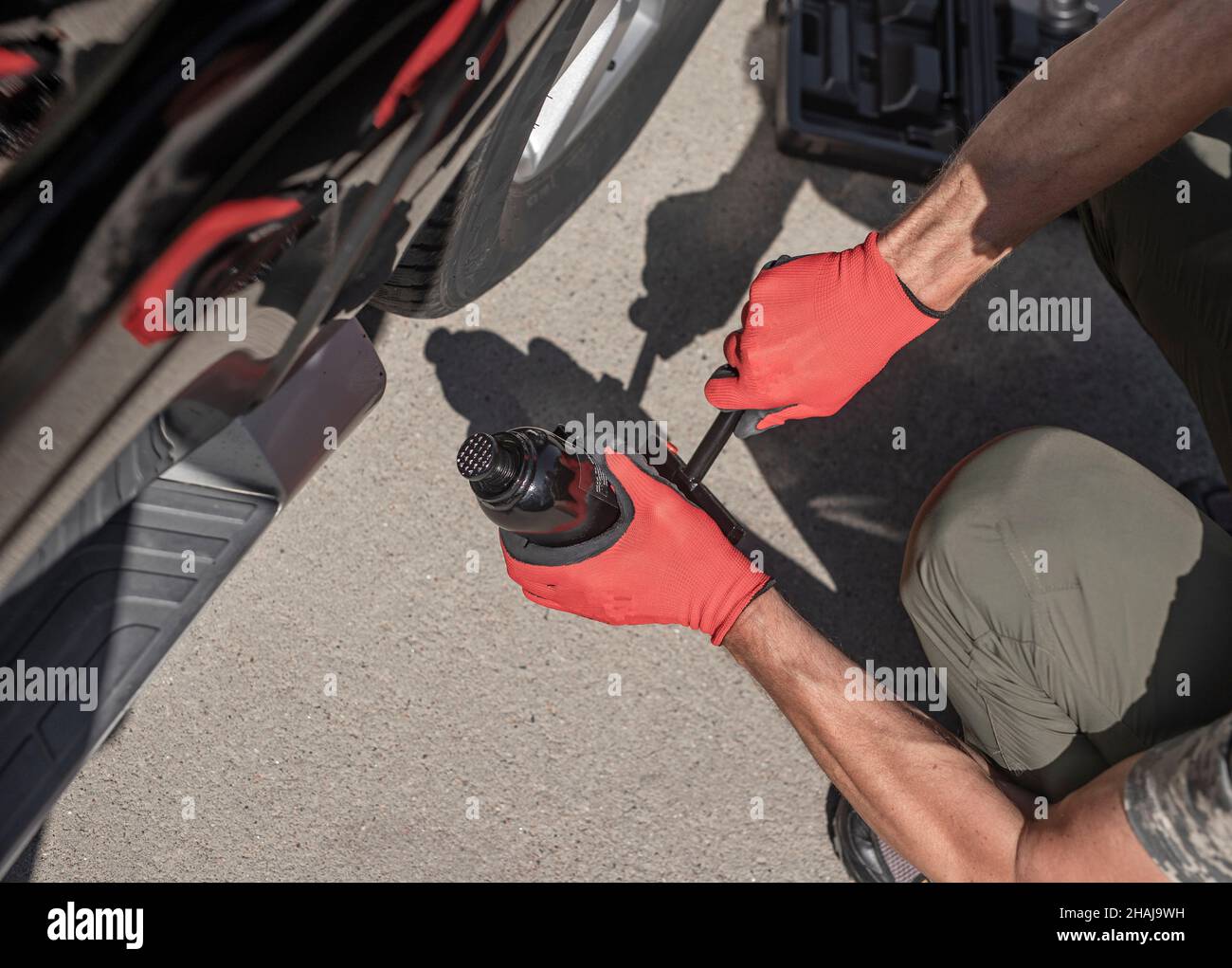 Hydraulic car jack is put under auto by male hands, top view. Stock Photo