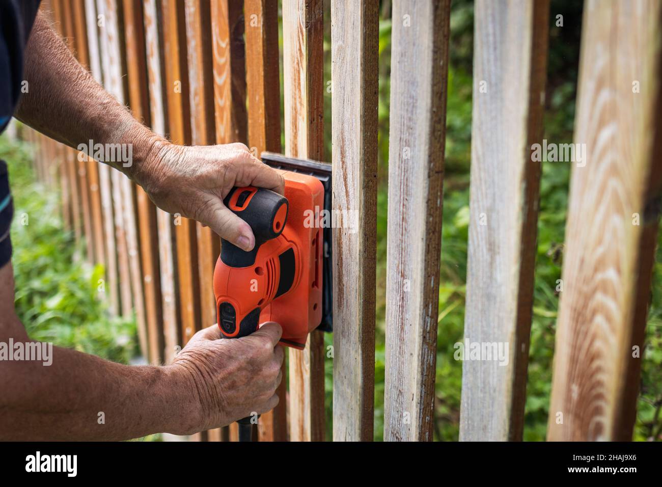 Sanding wooden picket fence. Electric vibrating power tool grinder. Sander in hands Stock Photo