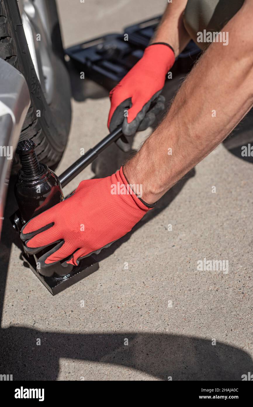 Hydraulick jack is put under car by male hands. Stock Photo