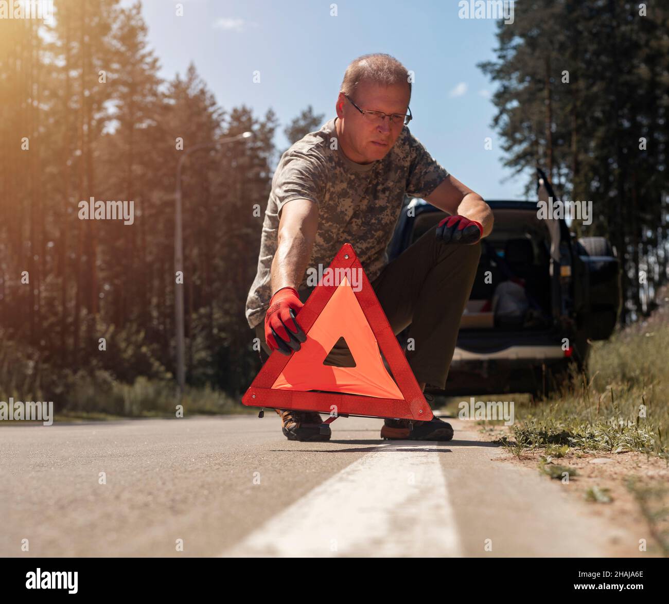 Driver putting red triangle caution sign on road near broken auto. Stock Photo