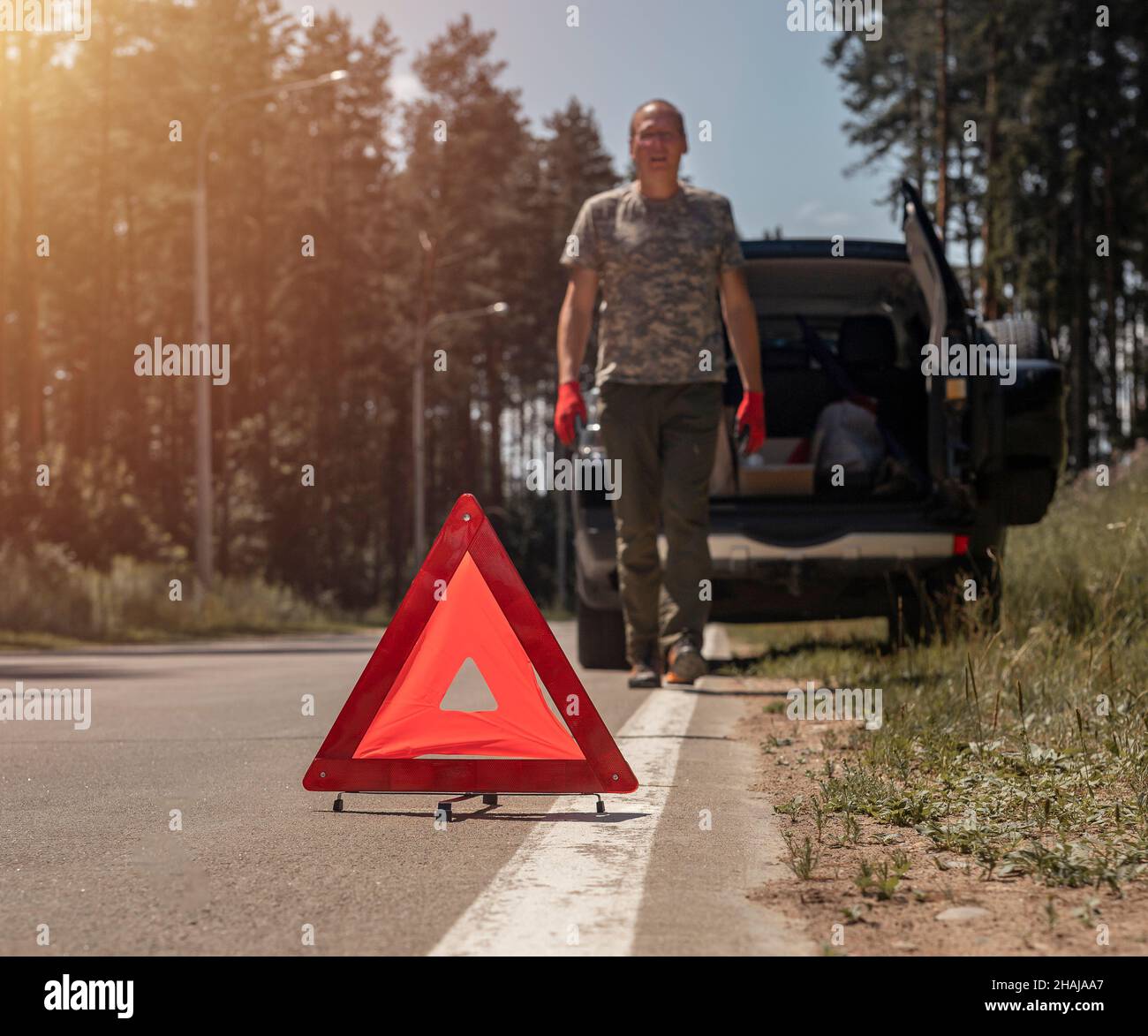 Triangle caution sign on road near broken car withdriver walking toward it. Stock Photo