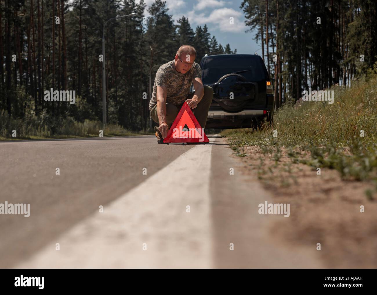 Driver man putting red triangle caution and warning sign on road near broken car. Stock Photo