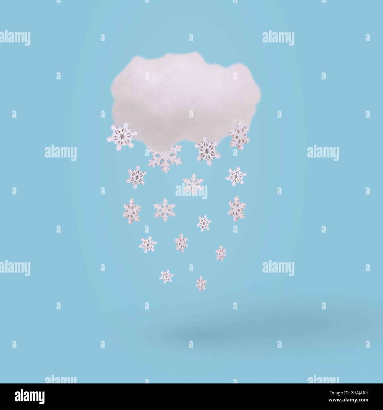 Creative concept with cloud and falling winter snowflake on bright blue background. Minimal winter holidays concept. Stock Photo