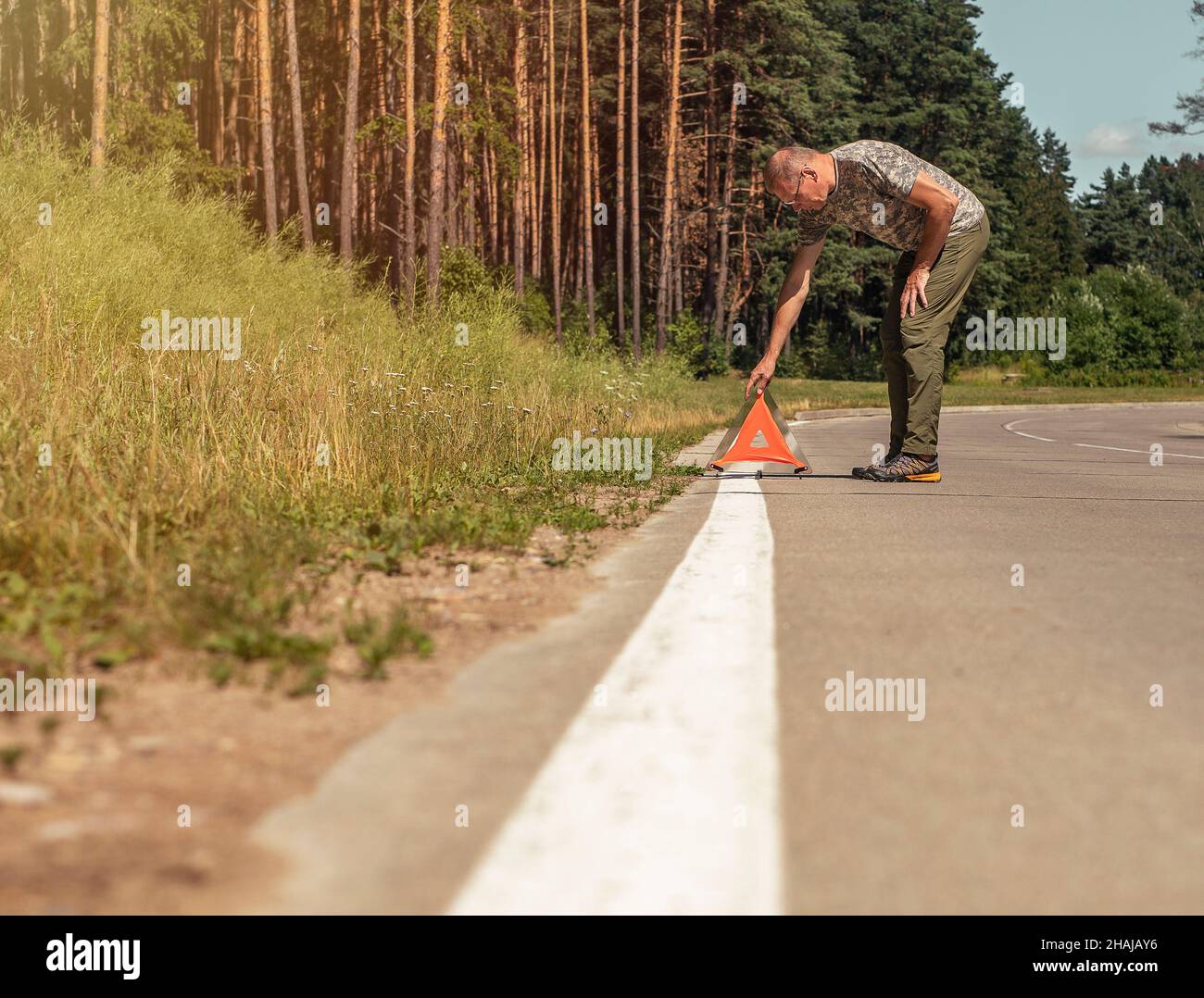 Man putting red triangle caution sign on road side in nature. Stock Photo