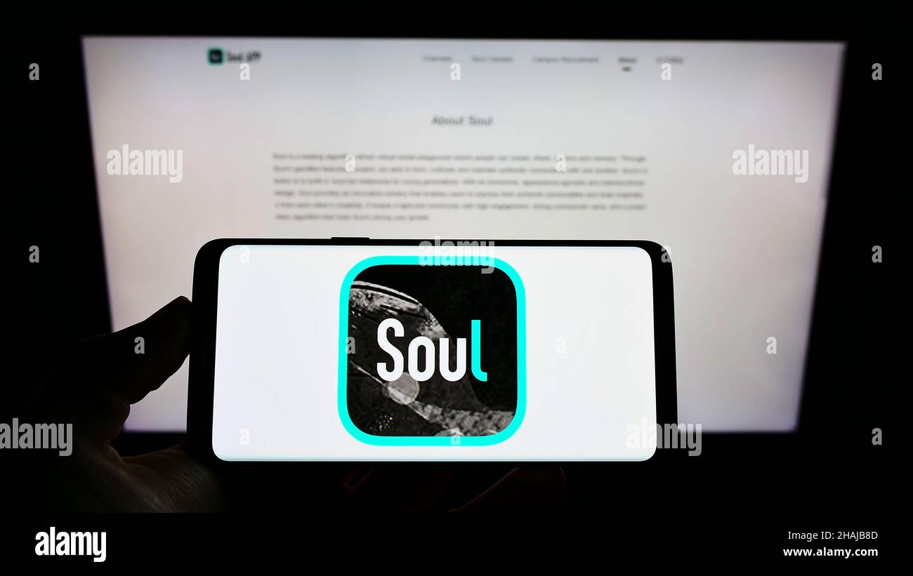 Person holding cellphone with logo of Chinese social network company Soulgate Inc. (Soul) on screen in front of web page. Focus on phone display. Stock Photo