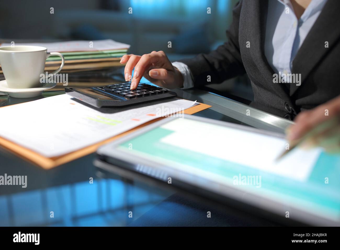 Businesswoman hand accounting using calculator and tablet on a desk in the night at office Stock Photo