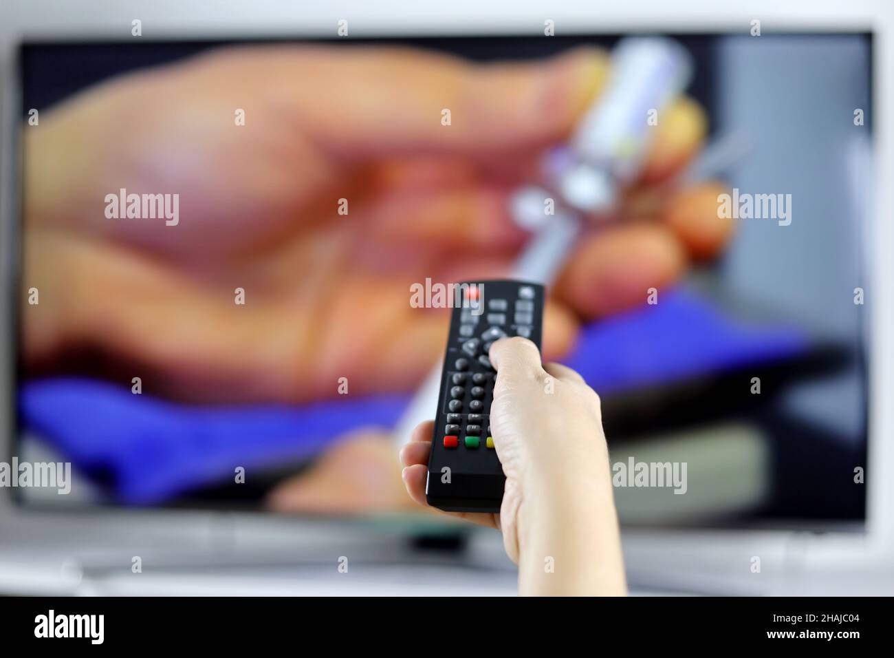 Female hand with remote control on TV screen background. Woman switches channels, watching medical program, news about coronavirus vaccination Stock Photo