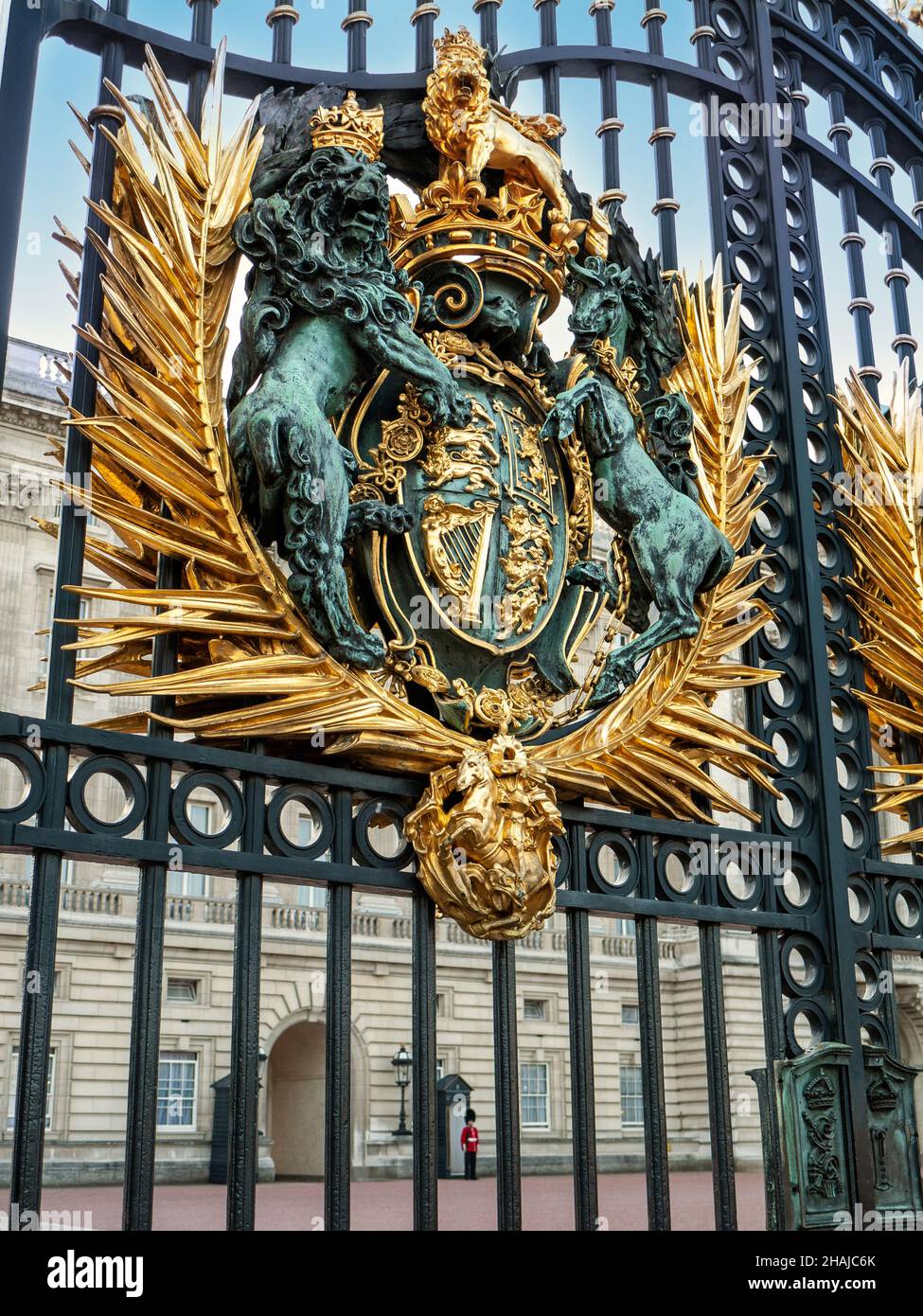 Royal crest on the entrance gates of Buckingham Palace with traditional guard in red tunic and busby in background, London, England Stock Photo